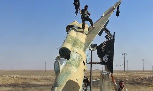 Isis fighters wave the group's flag from what is thought to a damaged a Syrian air force jet